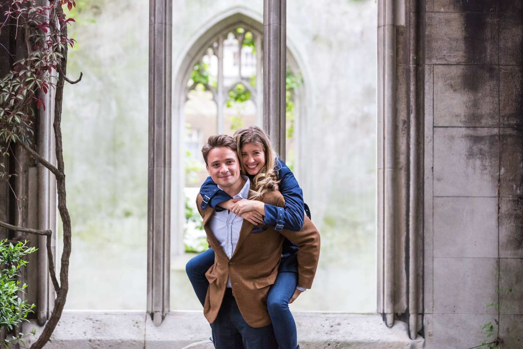 Oliver gives Paula a piggyback during their fun London engagement photoshoot in the beautiful gardens of St Dunstan-in-the-East