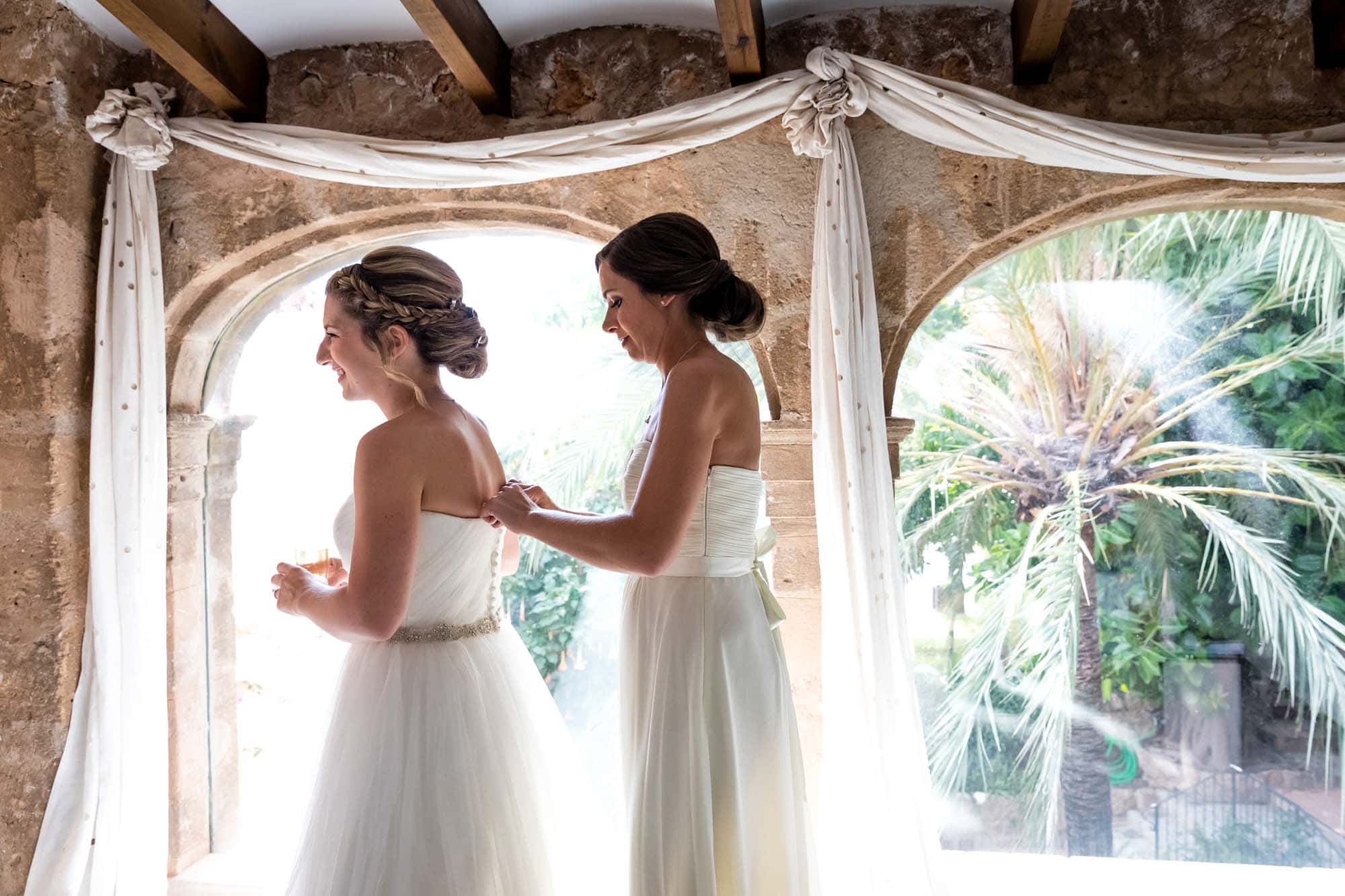 A bridesmaid helps the bride to put on her wedding dress at Hotel Can Vedera in Fornalutx