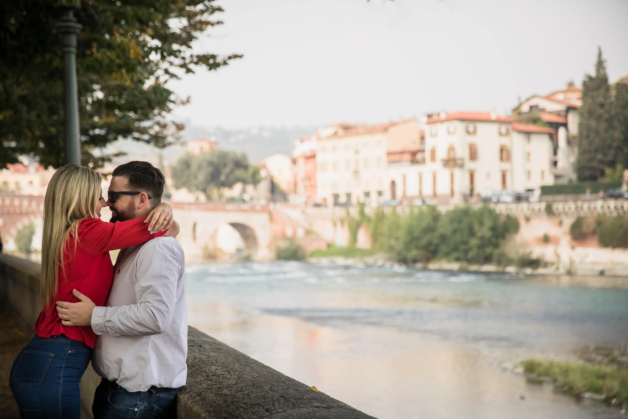 Engaged couple cuddle beside the River Adige in Verona, Italy