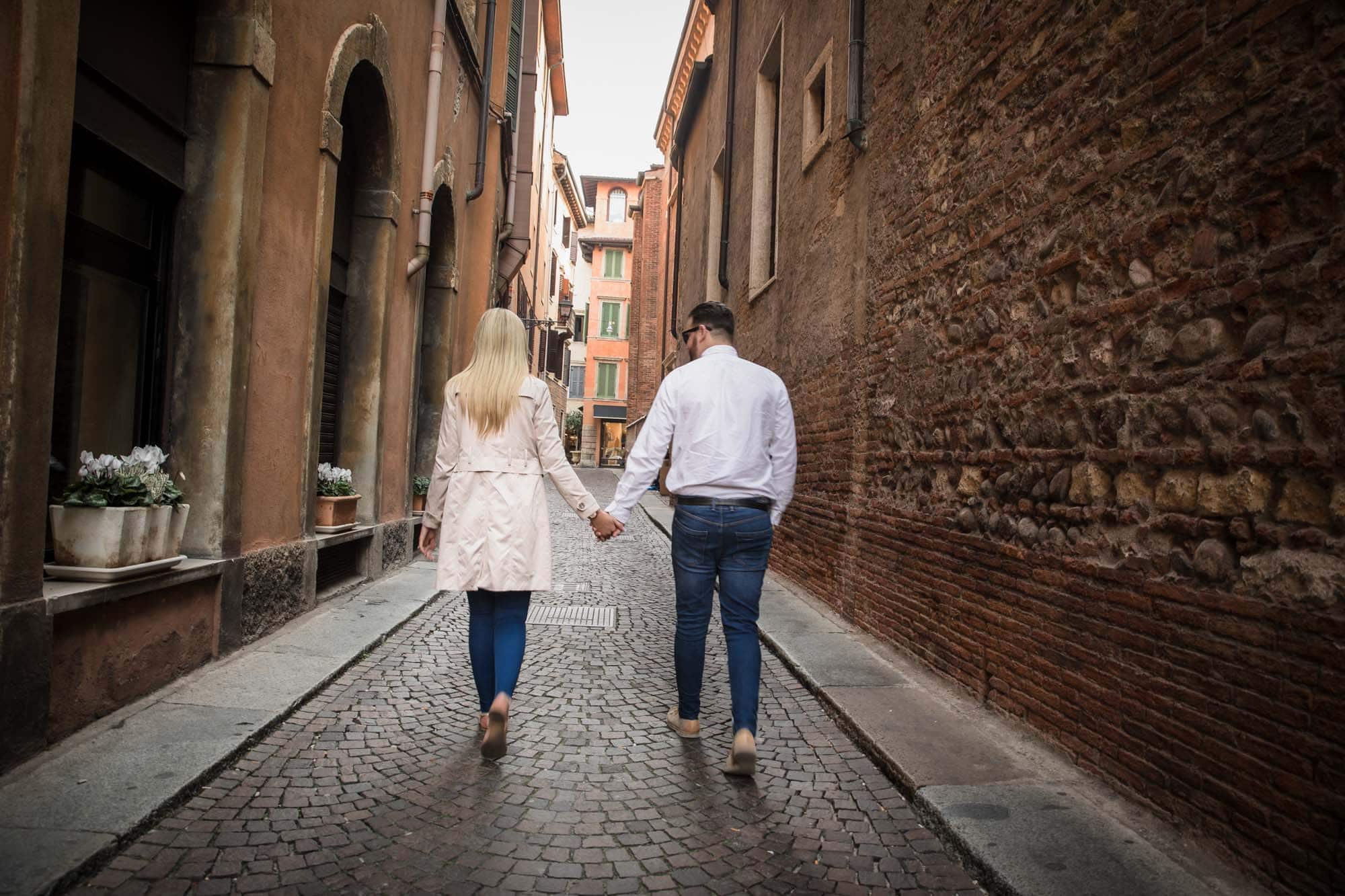 A couple in love hold hands through the back streets of Verona old town